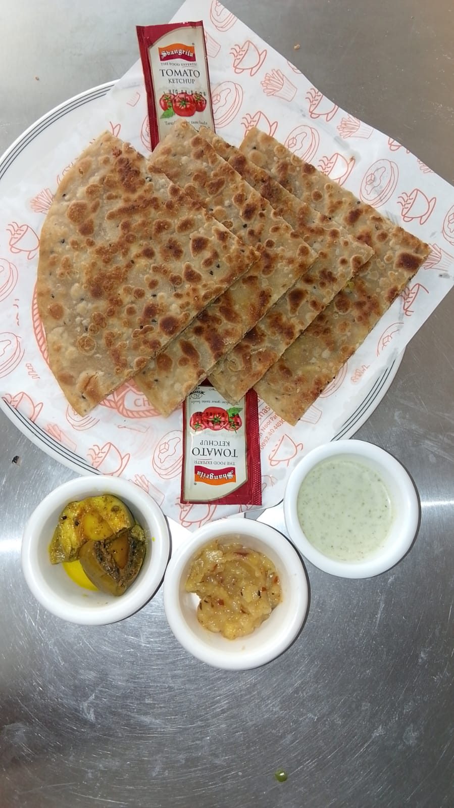 Whole paratha plated with pickle, chutney and mint raita