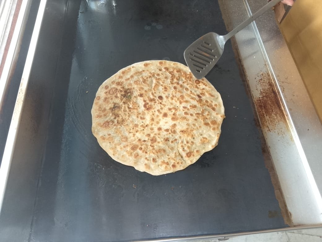 Paratha being flipped with a spatula on the hot tawa